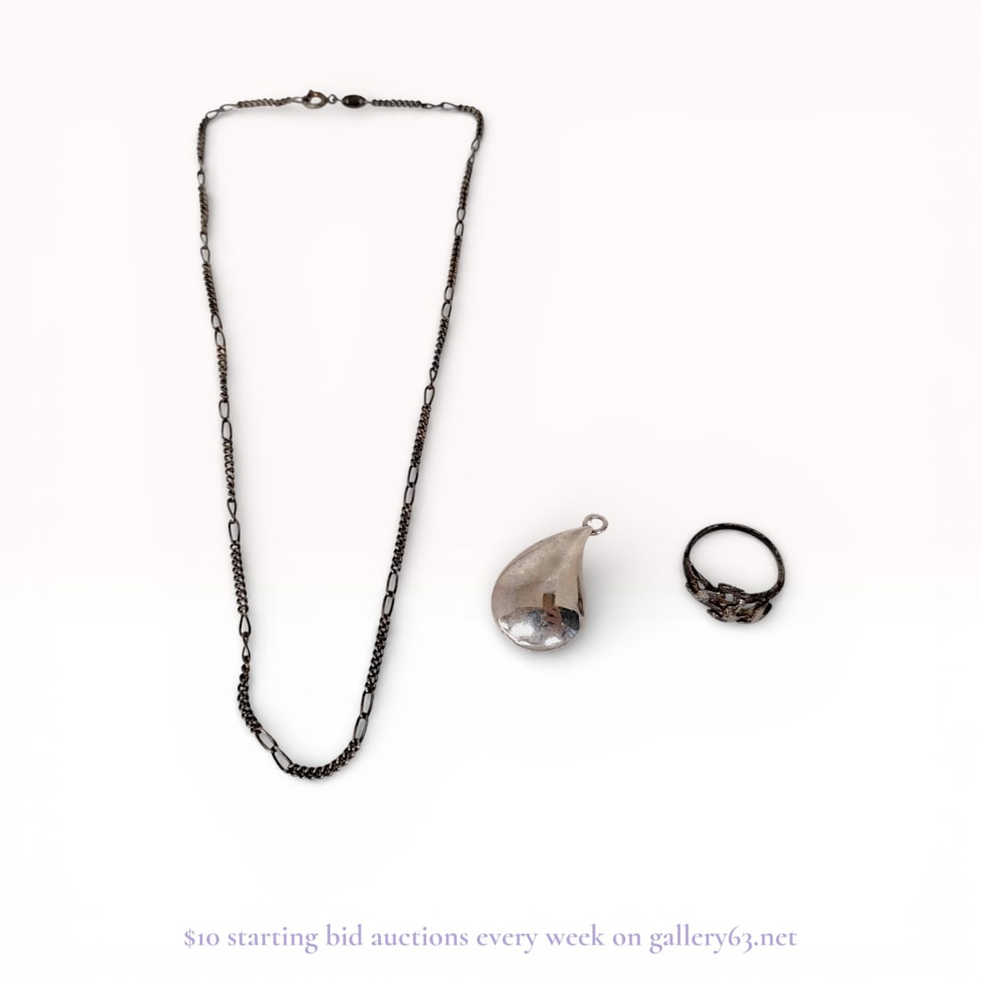 A Trio of Silver and Silver-Tone Jewelry Including a Figaro Chain, Teardrop Pendant, and Figural: A trio of silver and silver-tone jewelry pieces featuring a figural ring, a teardrop pendant, and a Figaro link chain. The sterling silver ring depicts birds in flight with an openwork band, while the