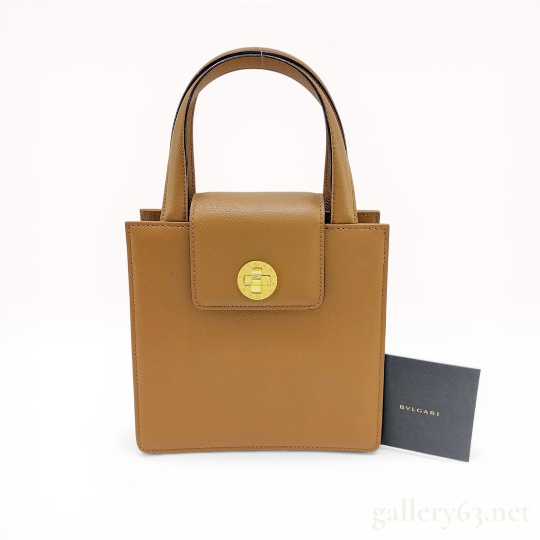 BVLGARI Grained Tan Leather Structured Top-Handle Bag: BVLGARI structured top-handle handbag crafted from tan grained calfskin leather featuring an accordion-style gusseted design. The bag is secured with a central gold-toned circular turn-lock closure an
