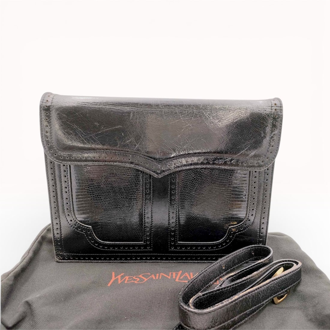 Yves Saint Laurent Vintage Brogue Detailed Accordion Shoulder Bag: Vintage Yves Saint Laurent accordion shoulder bag crafted from glossy black leather with lizard-embossed accent panels and perforated brogue trim. The interior is lined in reddish-brown leather and di