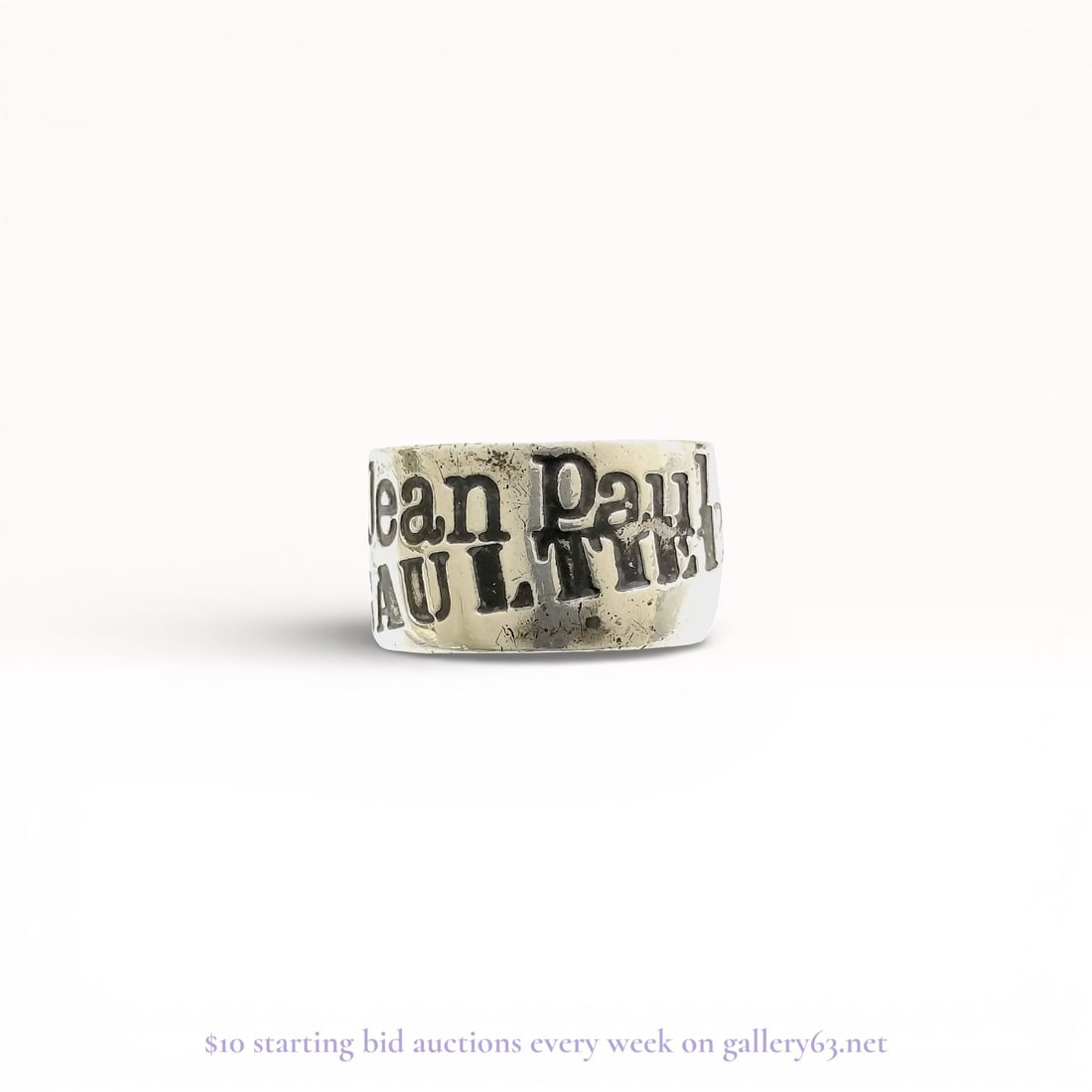 Jean Paul Gaultier Sterling Silver Logo Band Ring: Jean Paul Gaultier sterling silver logo band ring. The wide, flat-profile band features the designer name in bold relief block lettering across two offset rows. The interior of the band is incised wit