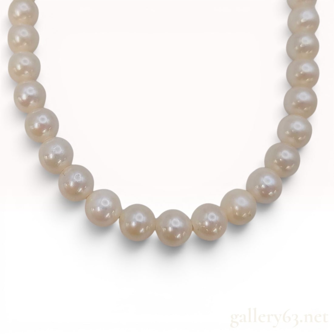 Long Cultured Pearl Necklace with Silver Filigree Clasp: A single-strand cultured pearl necklace featuring uniform pearls individually knotted on a white cord. The pearls exhibit a white to cream body color with high luster and round form. The necklace is s