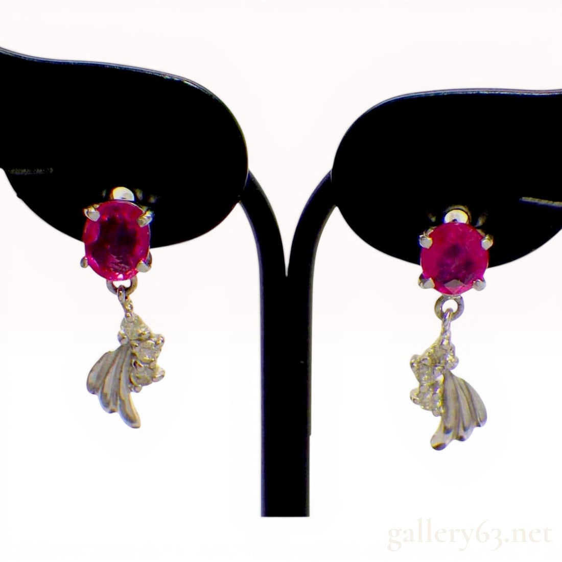 A Pair of 18K White Gold Ruby and Diamond Drop Earrings: A matched pair of 18K white gold drop earrings featuring oval mixed-cut natural ruby studs suspending stylized foliate drops set with round-cut diamonds. The rubies are heat treated for color enhancem