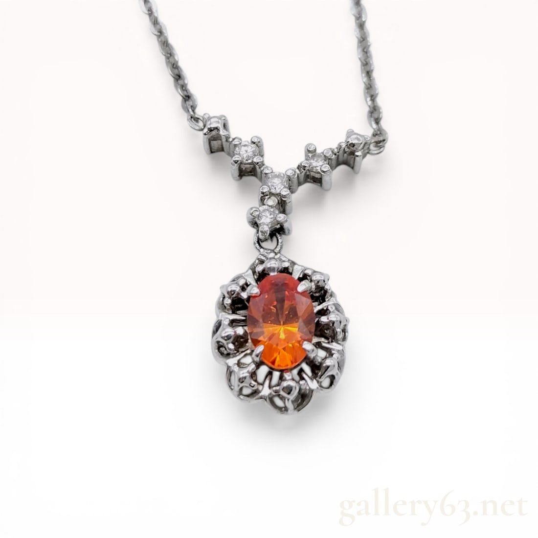 14 Karat White Gold Spessartite Garnet and Diamond Pendant Necklace: 14 karat white gold pendant necklace featuring a central 0.65 carat oval-cut orange spessartite garnet, set within a textured openwork frame. The pendant is suspended from a fixed Y-shaped bail accent