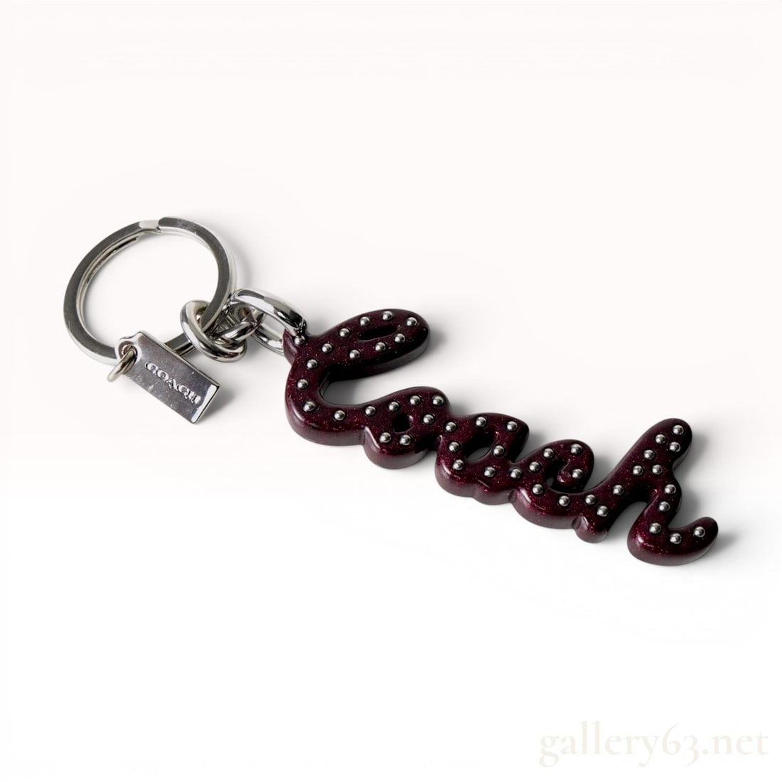 Coach Plum Glitter Resin Script Logo Keychain Bag Charm F76456: A Coach script logo keychain or bag charm, model F76456. The primary charm features the brand name Coach rendered in a cursive script. The charm is constructed from deep plum resin infused with fine g