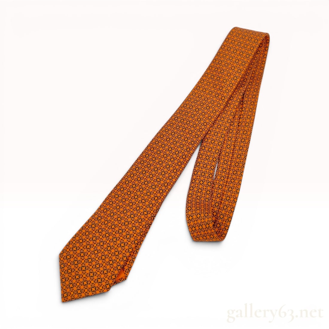 Hermes Orange Geometric H Circle Logo Silk Necktie: This necktie by Hermes is crafted from 100 percent silk and features a repeating interlocking circular geometric pattern in a dark charcoal tone set against the brand's signature orange ground. The co