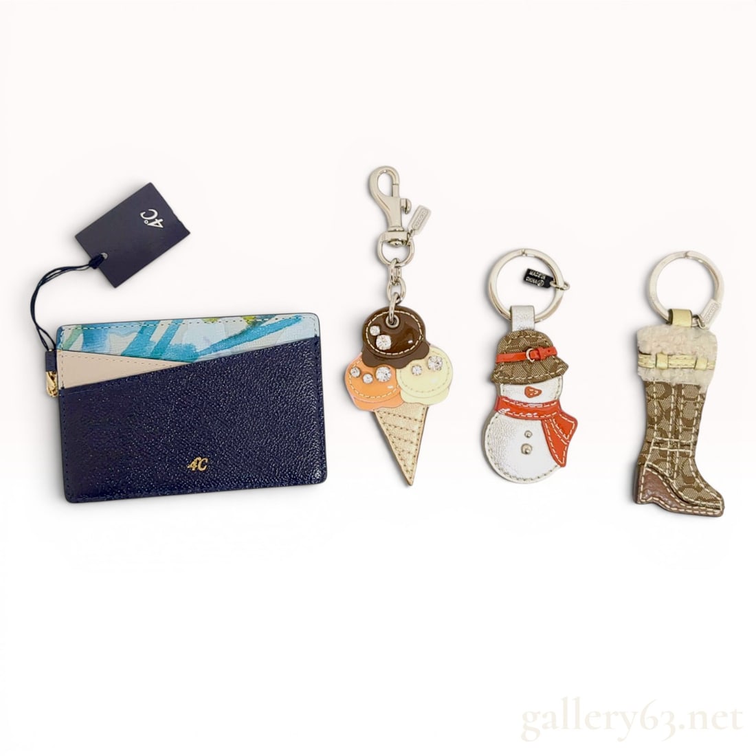 A Group of Designer Personal Accessories Including Coach Keychains and a 4C Card Holder w/Box: A group of designer personal accessories comprising a 4 C card holder and novelty keychains, including pieces by Coach. The card holder is crafted from navy blue pebbled leather with an ID window, whi