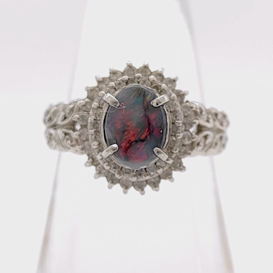 Platinum Natural Black Opal and Diamond Cocktail Ring: Platinum cocktail ring featuring a natural black opal center stone and a halo of natural diamonds. The oval cabochon opal is secured by four prongs within a tiered, scalloped diamond halo, flanked by 