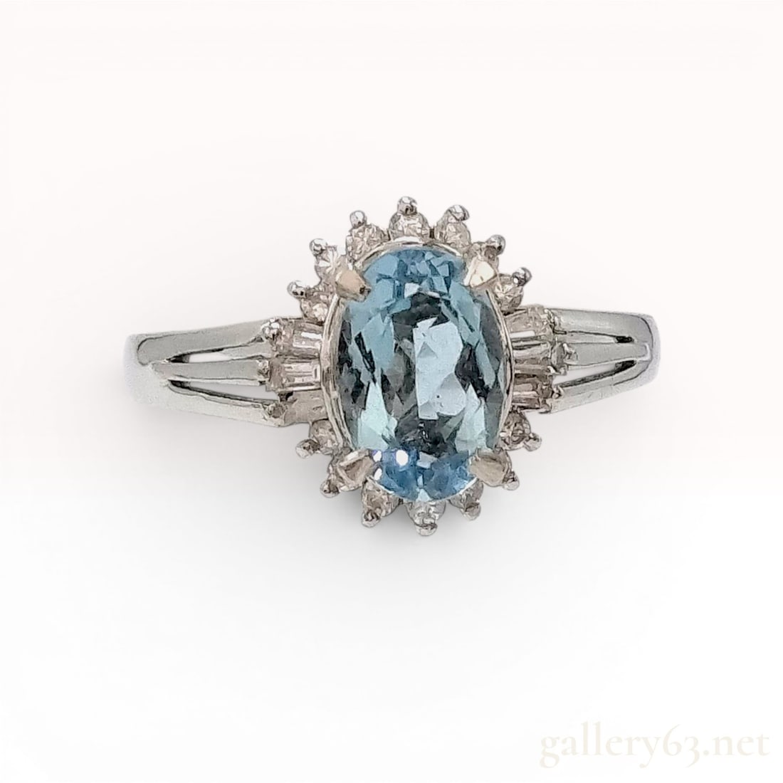 Platinum Oval 1.08ct Blue Topaz and Diamond Halo Ring: A platinum cocktail ring featuring a central oval-cut sky blue topaz weighing 1.06 carats. The gemstone is set within a four-prong mount and surrounded by a halo of round brilliant-cut diamonds. Each 
