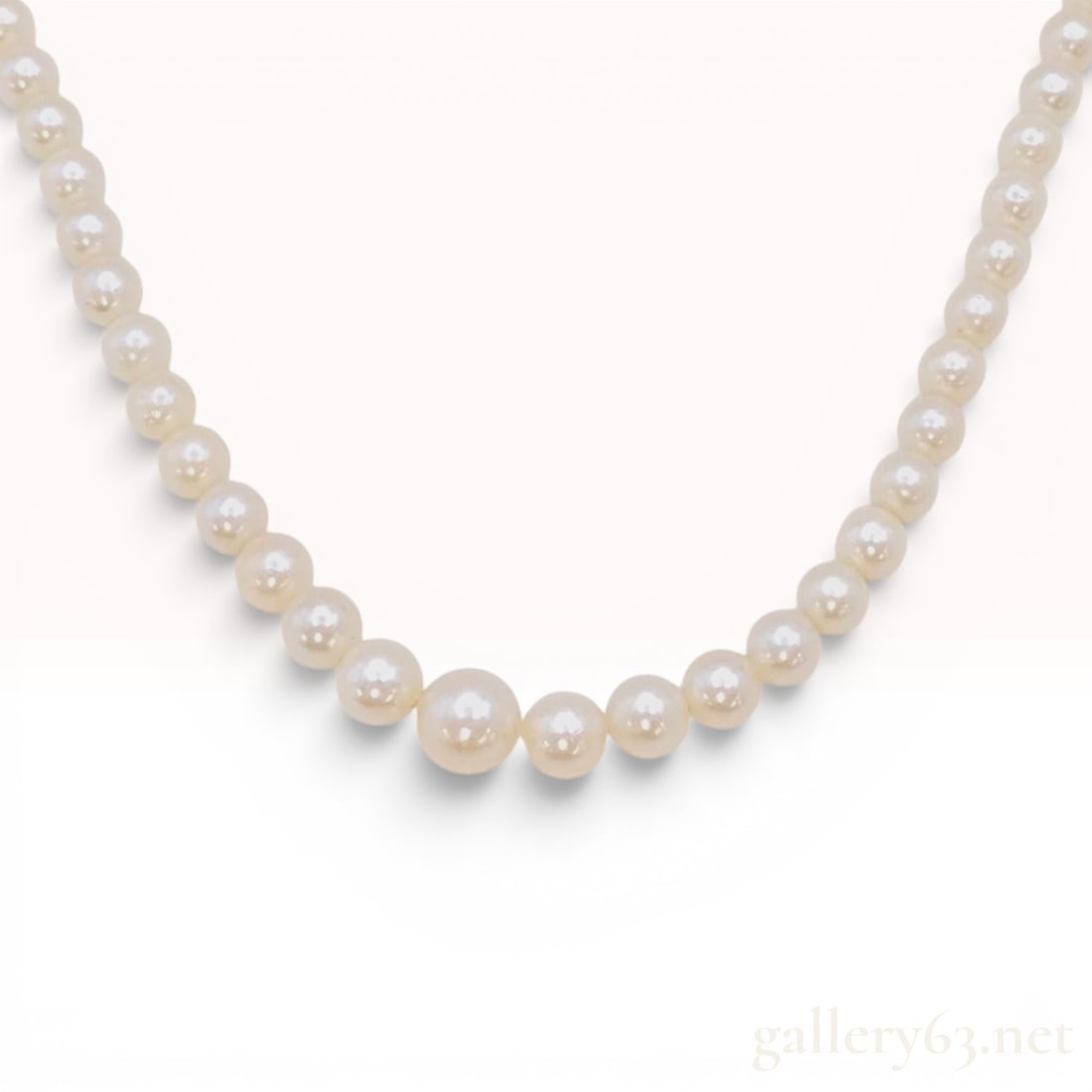 Vintage Graduated Semi-Round Pearl Necklace with Silver Clasp: A vintage single strand necklace composed of graduated semi-round pearls. The pearls display a cream hue with silvery-rose overtones and are hand-knotted on a white cord. The design features a graduat