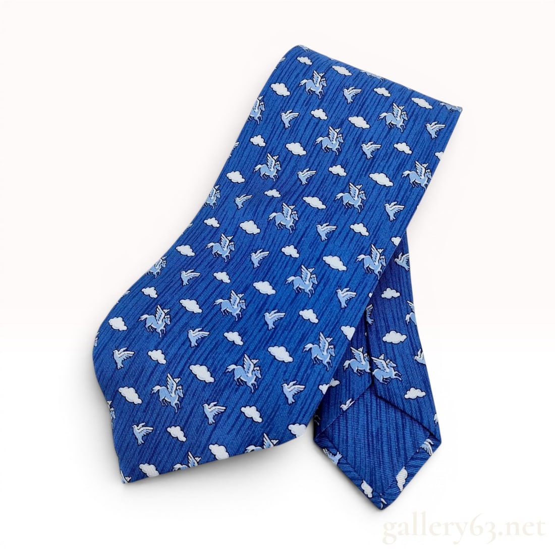 Hermes Blue Silk Pegasus and Dove Pattern Necktie: This Hermes men's necktie is constructed from blue ribbed silk and features a repeating pattern of light blue winged horses, white doves, and white clouds. The reverse of the wide blade is fitted with
