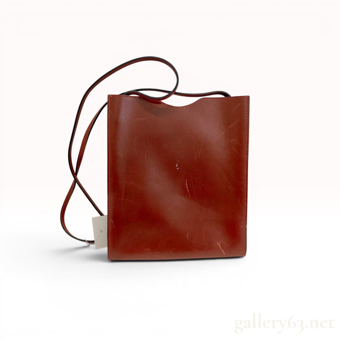 Hermes Onimaitou Leather Crossbody Bag: An Hermes Onimaitou crossbody bag crafted from smooth, reddish-brown leather. The minimalist design features a flat rectangular silhouette with a wide U-shaped cutout at the top opening and an integra