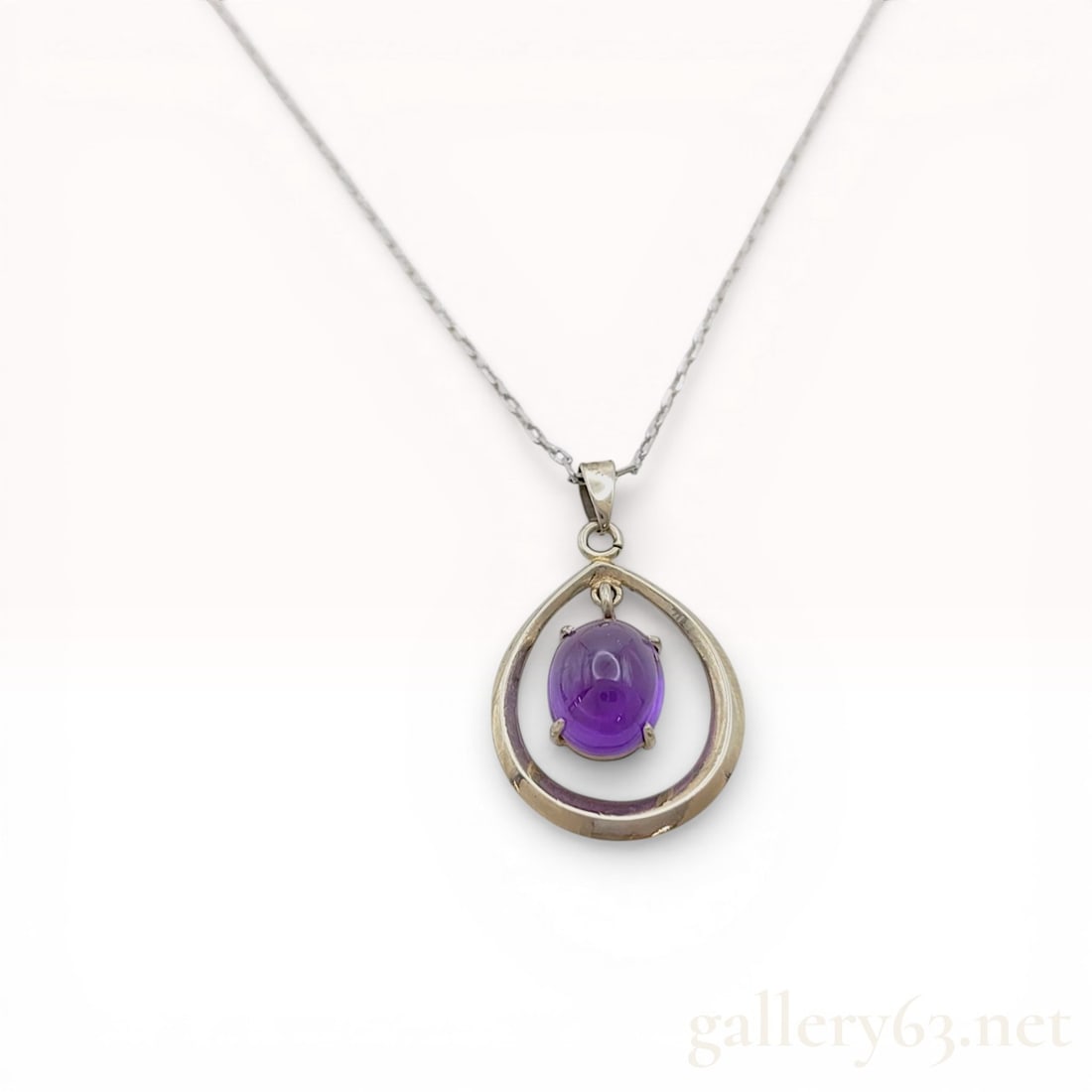 14 Karat White Gold and Amethyst Teardrop Pendant Necklace: 14 karat white gold pendant necklace featuring a natural oval cabochon amethyst. The open-work teardrop pendant suspends the gemstone in a four-prong setting from a fine cable link chain. The reverse 