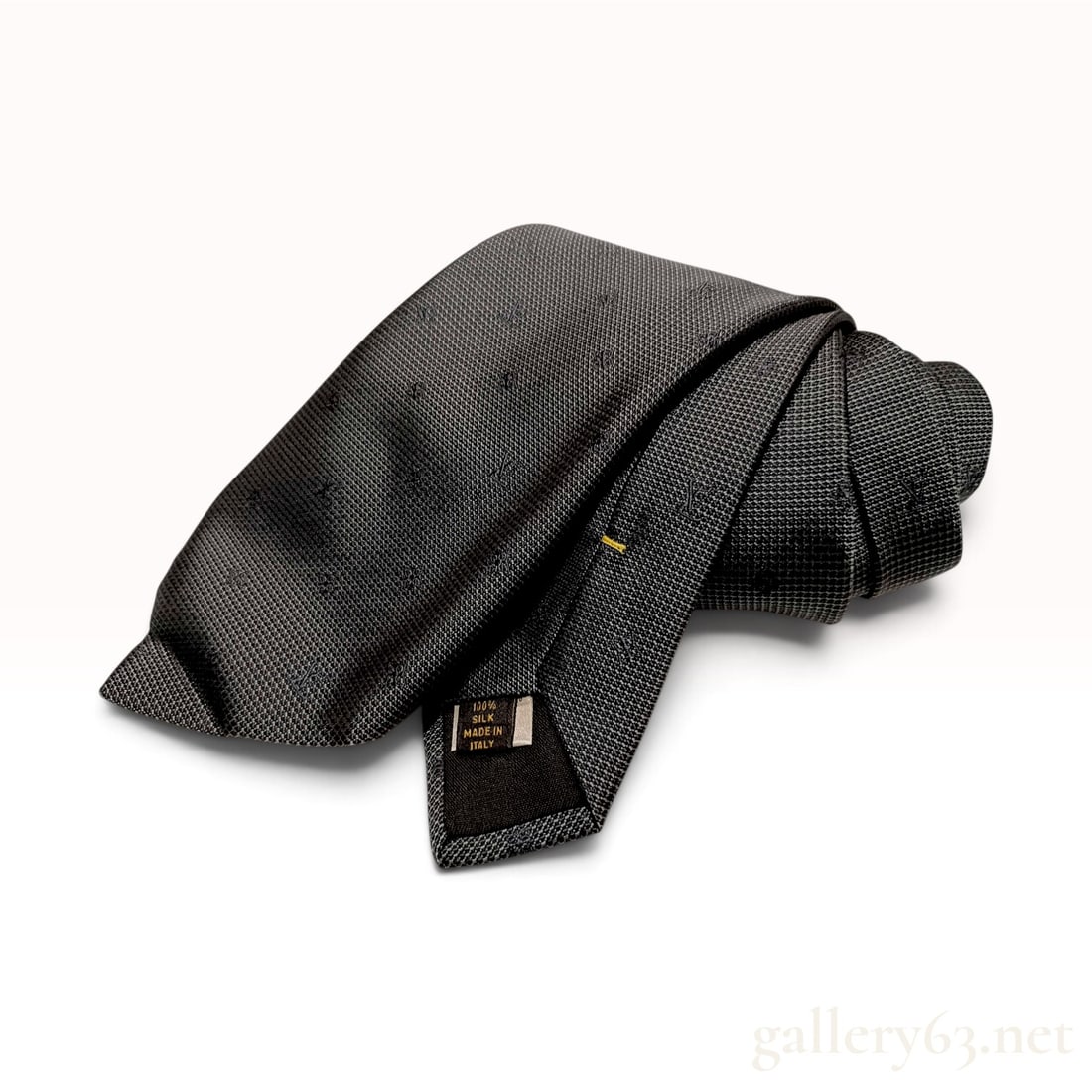 Louis Vuitton Men's Charcoal Gray Tonal Monogram Silk Necktie: A Louis Vuitton necktie crafted from charcoal gray silk featuring a micro-textured bird's eye weave. The fabric is decorated with a tonal jacquard-woven LV monogram pattern throughout. The reverse of 