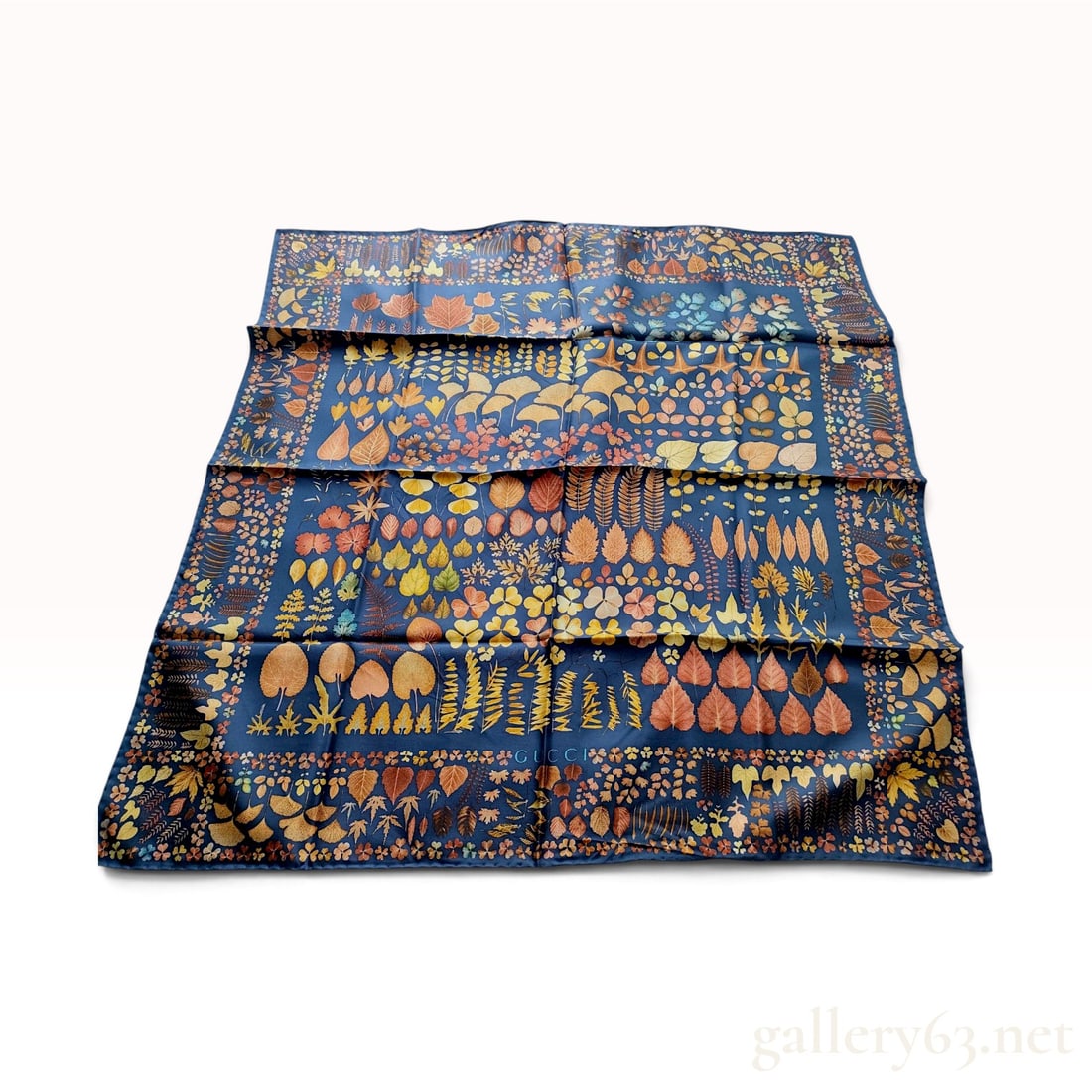 Gucci Navy Blue Silk Scarf with Autumnal Leaf Pattern: This Gucci square scarf is crafted from 100 percent silk and features an intricate botanical leaf motif. The design displays various leaf species, including ginkgo, maple, clover, and ferns, in a pale