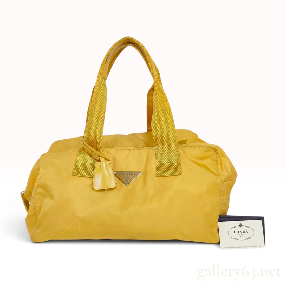 Prada Yellow Tessuto Nylon Small Duffle Bag: This Prada handbag features a yellow nylon body in a classic Boston or small duffle silhouette. The bag is equipped with double flat yellow webbing top handles that transition into rounded yellow leat