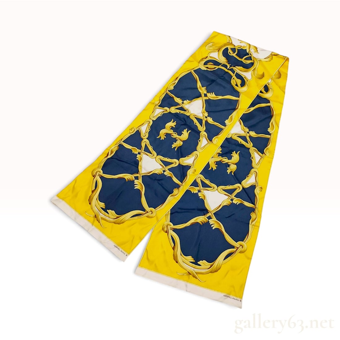 Hermes Silk Maxi Twilly Scarf in Yellow and Navy Blue: An authentic Hermes Paris silk Maxi Twilly scarf featuring a classical baroque design of scrolling gold acanthus leaves. The ornate foliage forms circular medallion frames against a navy blue ground w