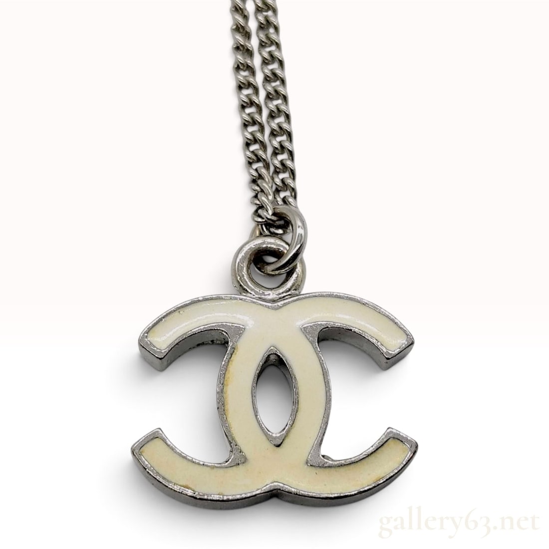 Chanel 2007 Continuous Collection Enamel CC Logo Pendant Necklace: A Chanel costume jewelry necklace featuring the iconic interlocking CC logo pendant. The pendant is constructed from silver-tone metal with a white enamel inlay. It is suspended from a fine curb link 