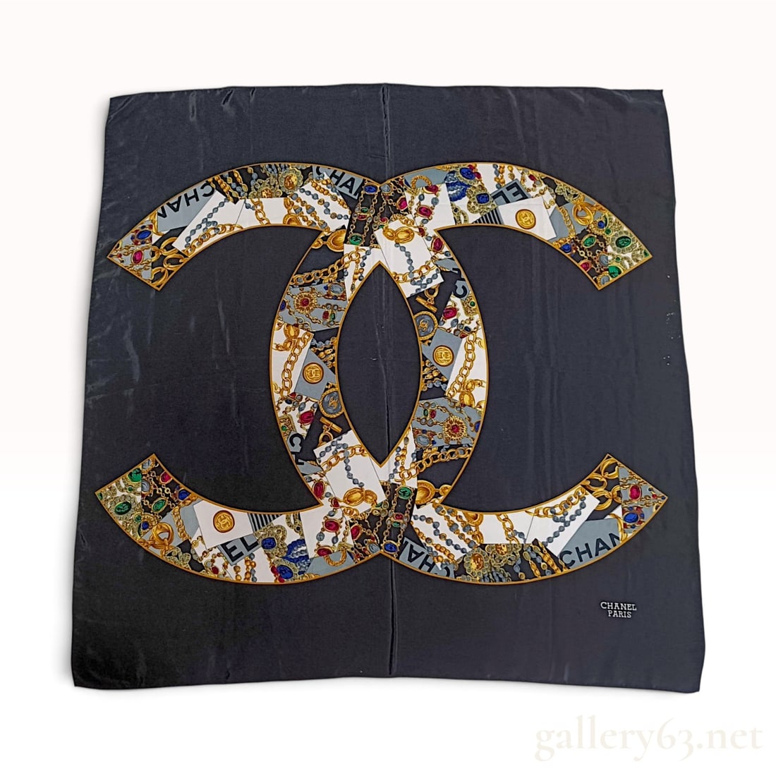 Chanel Vintage Navy Blue Silk Scarf with Interlocking CC Jewelry Motif: A vintage silk scarf from Chanel featuring a large central interlocking CC logo positioned on a solid navy blue ground. The logo interior is filled with a detailed collage pattern depicting signature 