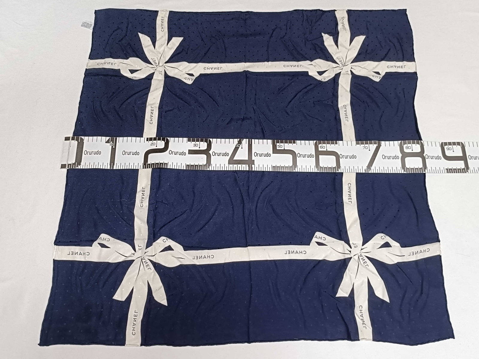 Chanel Navy Blue Silk Bow Motif Square Scarf: A Chanel square silk scarf featuring a navy blue ground with a repeating woven jacquard diamond pattern. The printed design consists of wide white ribbons tied into bows at the four corners, creating 