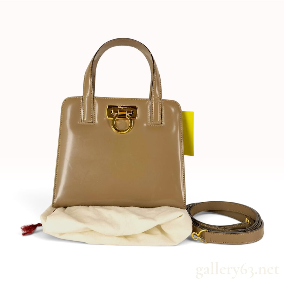 Salvatore Ferragamo Gancini Top Handle Bag in Taupe Patent Leather: Salvatore Ferragamo Gancini top handle handbag in taupe patent leather. This structured bag features dual rolled top handles and a front flap closure. The exterior is accented with a gold-tone metal G