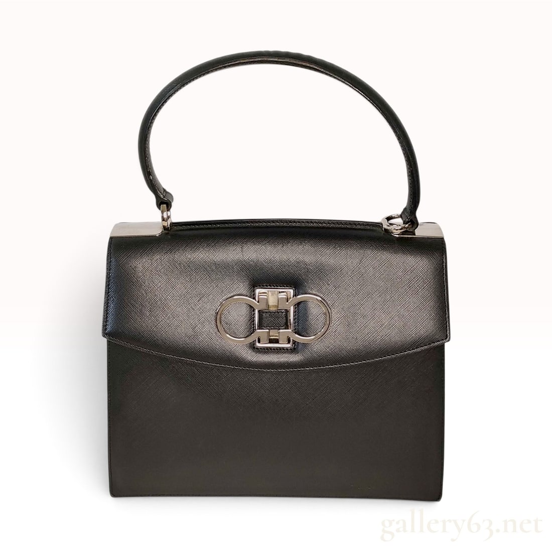 Salvatore Ferragamo Gancini Black Saffiano Leather Top Handle Bag: This Salvatore Ferragamo Gancini top handle bag is crafted from black Saffiano leather with a structured trapezoidal silhouette and a single rolled top handle. The exterior features a signature silver