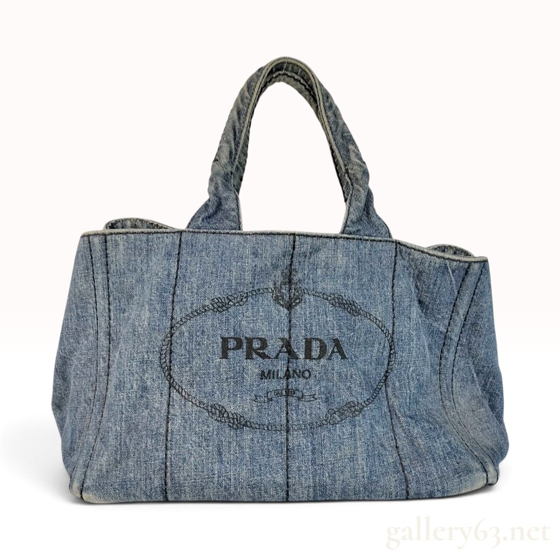 Prada Canapa Light Blue Denim Tote Bag: This Prada Canapa tote bag is crafted from light blue acid-washed denim featuring black contrast topstitching. The front panel is detailed with a black screen-printed PRADA MILANO logo contained withi