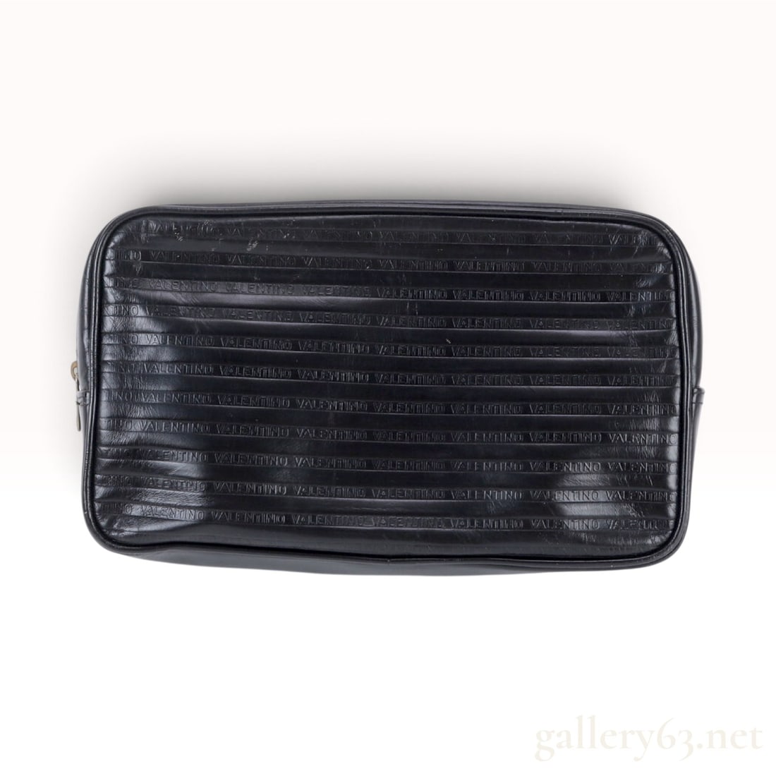 Vintage Mario Valentino Black Embossed Leather Pouch: This Mario Valentino travel bag crafted from black leather features two main panels with repeating horizontal rows of the word VALENTINO embossed into the surface. The sides and base are constructed f