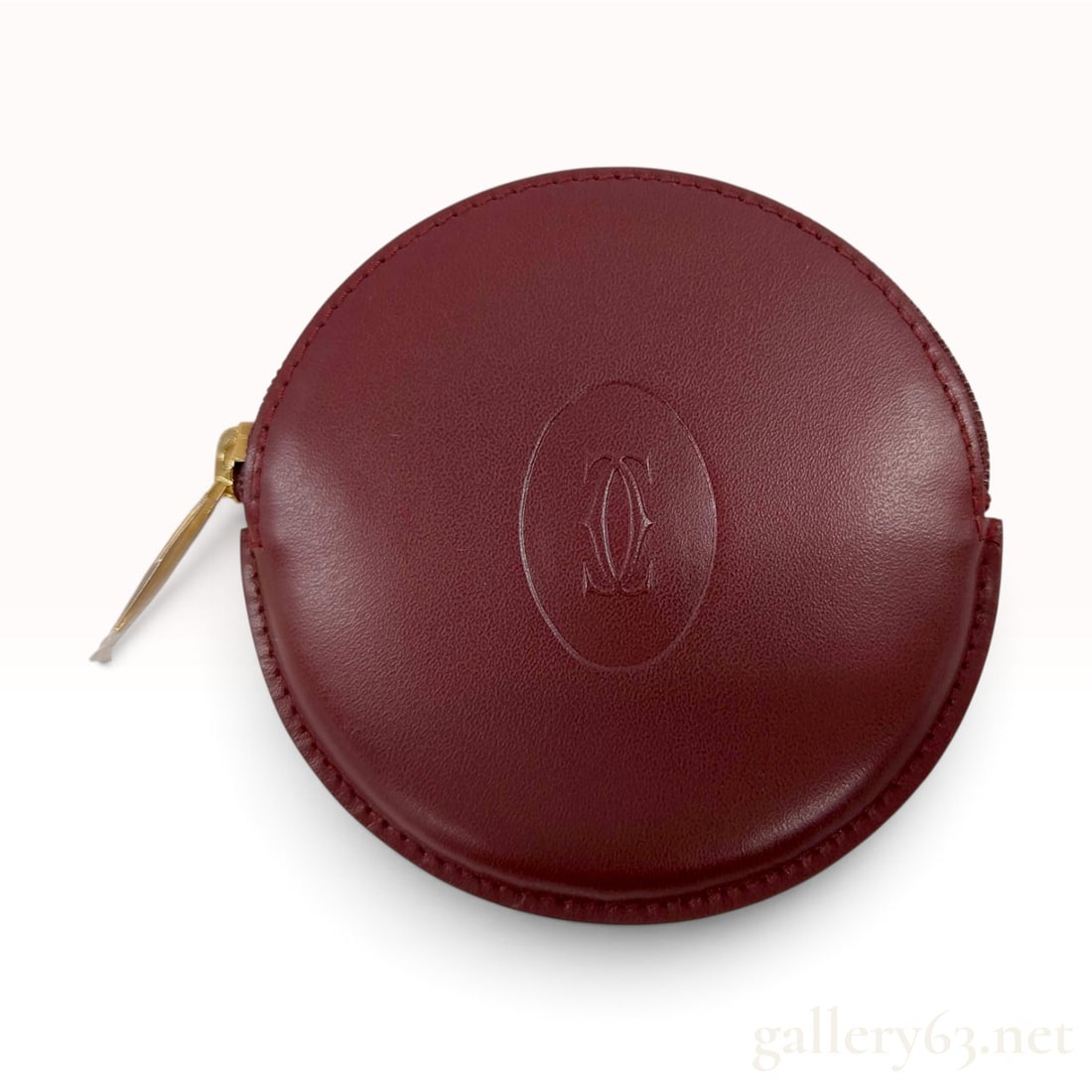 Vintage Cartier Must de Cartier Bordeaux Grained Leather Circular Coin Pouch: This Cartier circular coin pouch is crafted from bordeaux grained calf leather in the Must de Cartier style. The exterior features an embossed oval medallion centered on the front face containing an