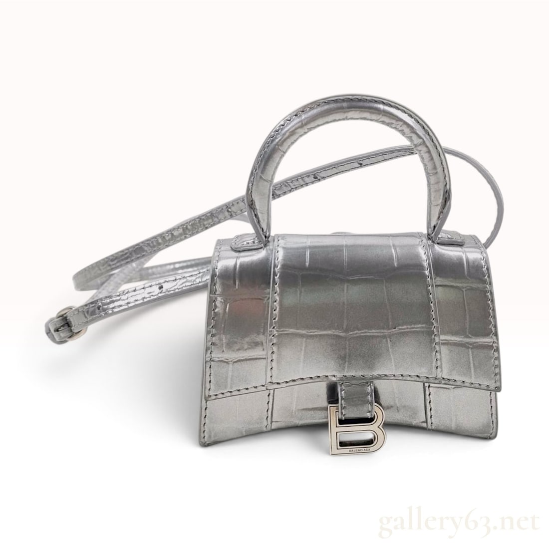 Balenciaga Hourglass XS Silver Metallic Croc-Embossed Calfskin Top Handle Bag: This Balenciaga Hourglass XS top handle bag is crafted from silver metallic calfskin leather featuring a crocodile-embossed finish. The design is characterized by a signature curvilinear base and a