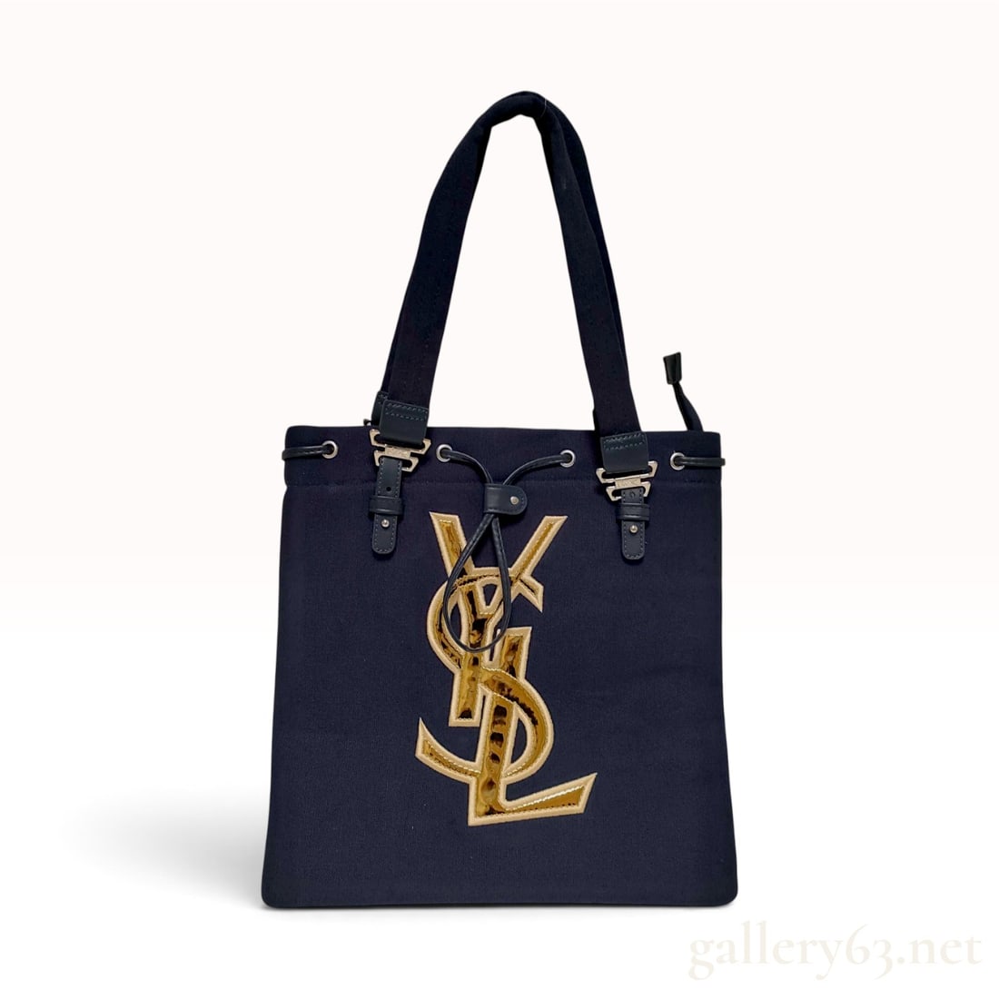 Yves Saint Laurent Navy Canvas Monogram Tote Bag: This Yves Saint Laurent tote bag is crafted from heavy-duty navy blue canvas. The front is dominated by a large, interlocking YSL monogram applique featuring a gold-toned, animal-print-textured reflec
