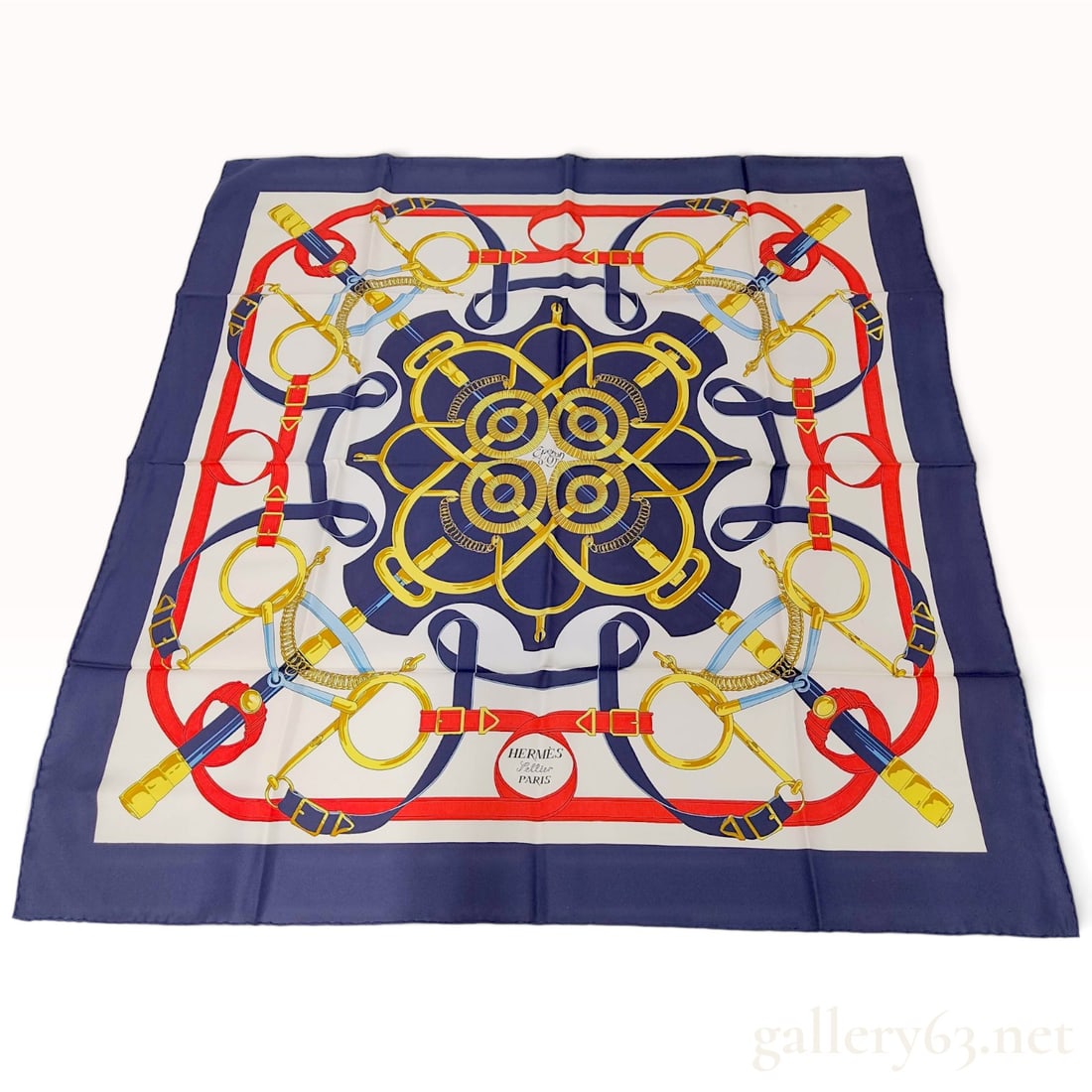 Hermes Eperon d'Or Navy Silk Carre 90: This Hermes silk carre 90 in the Eperon d'Or pattern is crafted from silk twill and was designed by Henri d'Origny. The equestrian theme features a symmetrical arrangement of overlapping stirrup leath