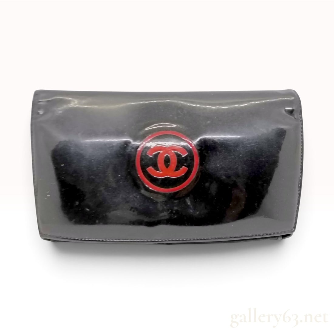 Vintage Chanel Patent CC Trousse Maquil Black Patent Leather Wallet 19 cm: A vintage Chanel Patent CC Trousse Maquil wallet crafted from black patent leather. The exterior features a prominent embossed circular emblem at the front center containing a red interlocking CC logo