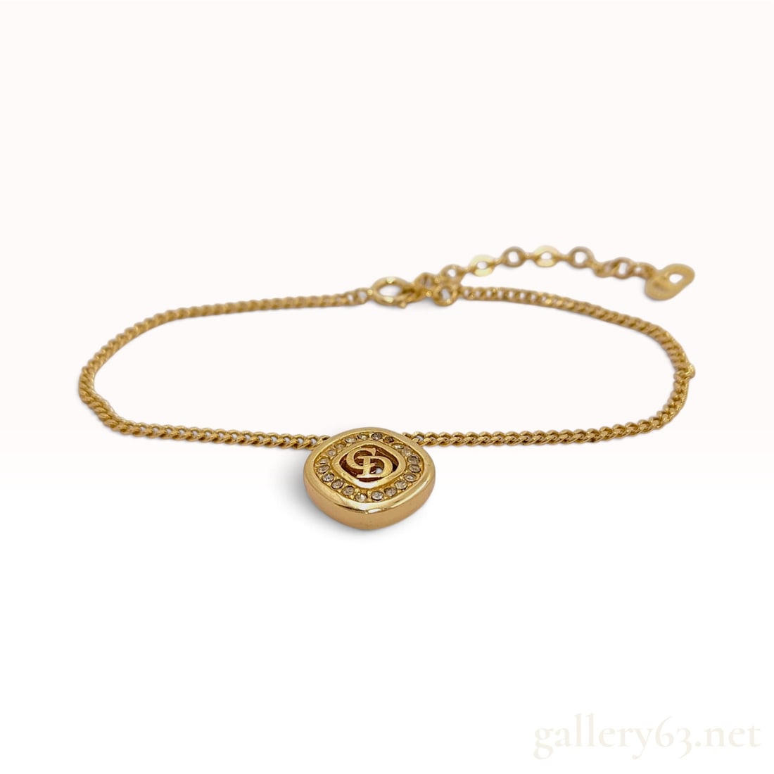 Vintage Christian Dior CD Logo Gold Toned Curb Link Bracelet: A Christian Dior curb link bracelet crafted from gold-toned metal featuring a central circular pendant. The pendant showcases a raised CD monogram surrounded by a halo of small, clear round faceted rh