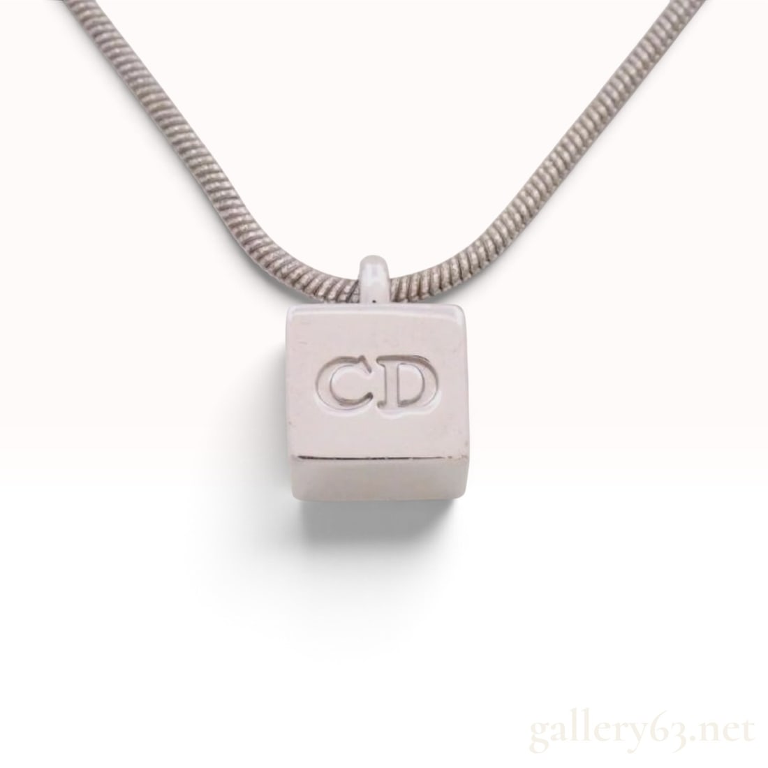 Vintage Polished Metal CD Monogram Cube Pendant Necklace: A pendant necklace featuring a polished cube pendant with an incised CD monogram on one face. The pendant is suspended from a flexible snake chain. The necklace is secured by a lobster claw clasp and 