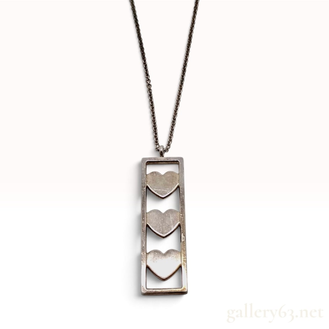 Tiffany & Co. Triple Heart Bar Sterling Silver Pendant Necklace: This Tiffany & Co. pendant necklace is crafted from sterling silver and features a vertical rectangular bar pendant with three tiered, cut-out heart motifs. The pendant is suspended from a fine cable 