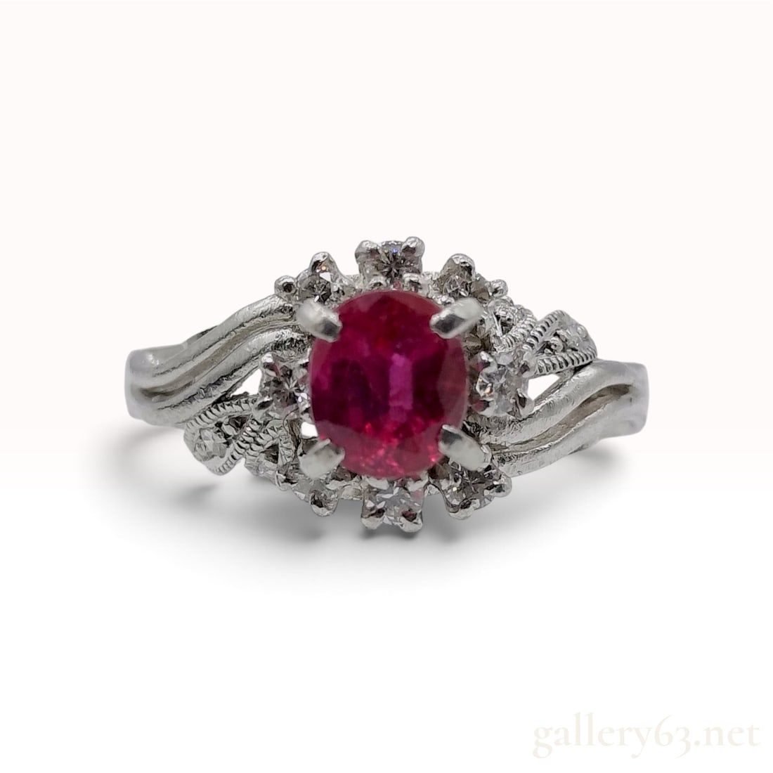 A Vintage Platinum 0.62ct Ruby and 0.21ctw Natural Diamond Cocktail Ring: This Platinum cocktail ring is crafted with an oval-cut pinkish-red ruby and numerous natural diamond accents. The center 0.62ct ruby is held in a four-prong setting atop a raised, tiered basket. The 