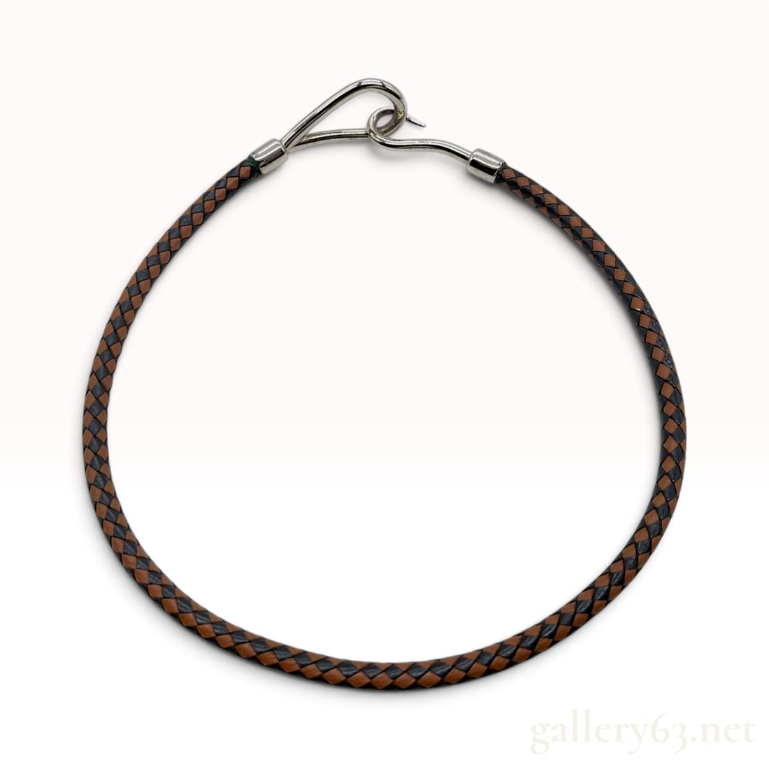 Hermes Jumbo Brown and Black Braided Leather Necklace: This Hermes Jumbo necklace is crafted from a round, two-tone braided leather cord in a woven pattern of brown and black. The design features a silver jumbo hook-and-eye clasp with the hook terminal in