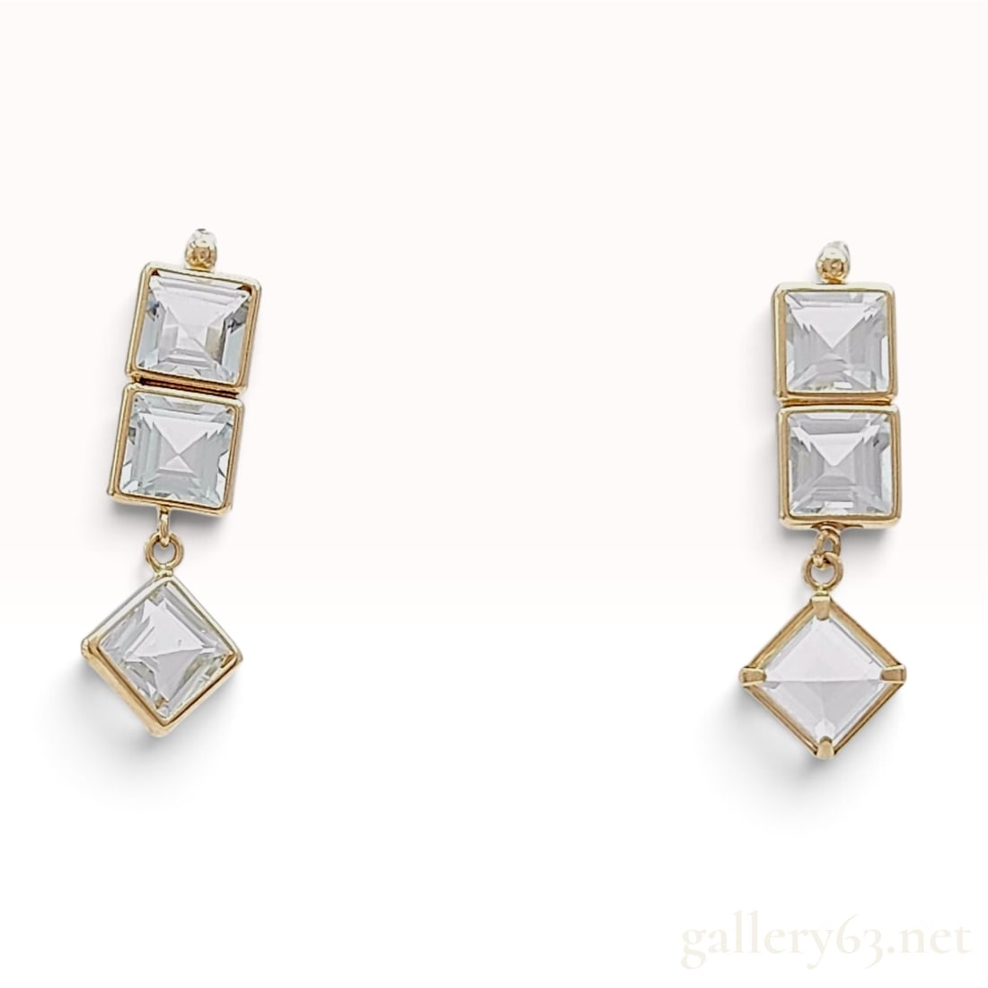 A 10 Karat Yellow Gold and 1.78ctw Clear Gemstone Drop Earrings: This matched pair of drop earrings is crafted from 10 karat yellow gold. Each earring features a linear arrangement of three square-cut clear gemstones with step-cut faceting. The top two gemstones ar