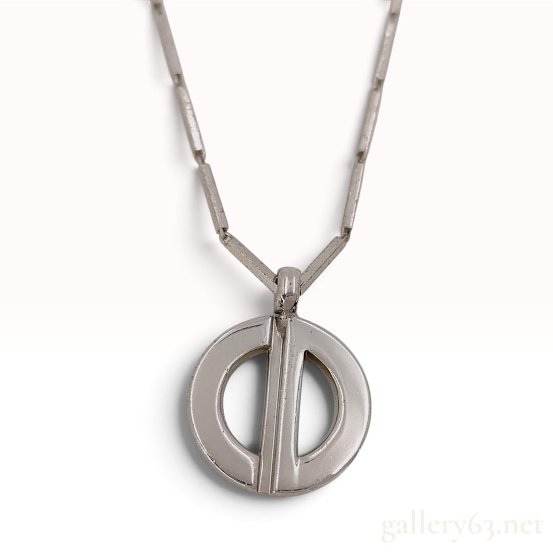 Vintage Christian Dior Modernist Pendant Necklace: This Christian Dior pendant necklace features a modernist aesthetic centered on a circular openwork pendant with a vertical bar. The pendant is suspended from a bar-link chain composed of cylindrical 