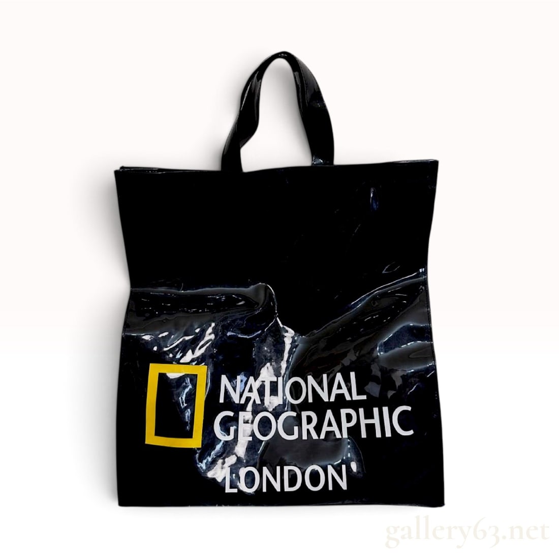 National Geographic London Glossy Black Logo Tote Bag: This National Geographic London tote bag is constructed from a high-gloss black vinyl material. The exterior features a prominent yellow rectangular logo above the printed white characters NATIONAL GE