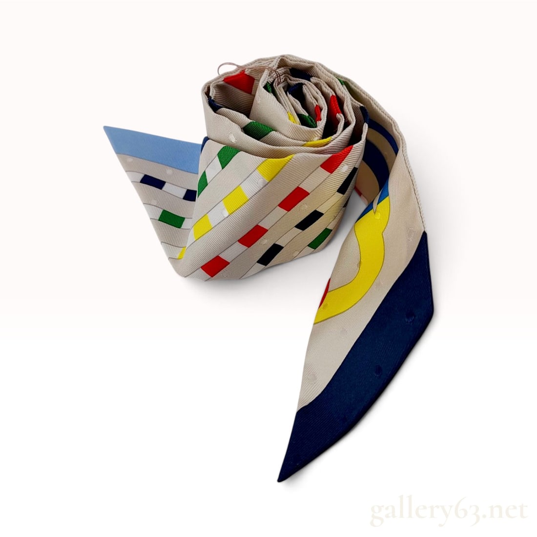 Hermes Bouclerie Moderne Plumetis Craie/Bleu/Rouge Silk Twilly with Retail Tag: This Hermes twilly is crafted from silk in the Bouclerie Moderne pattern featuring a plumetis texture of raised woven dots throughout the fabric. The design showcases stylized interlocking geometric s
