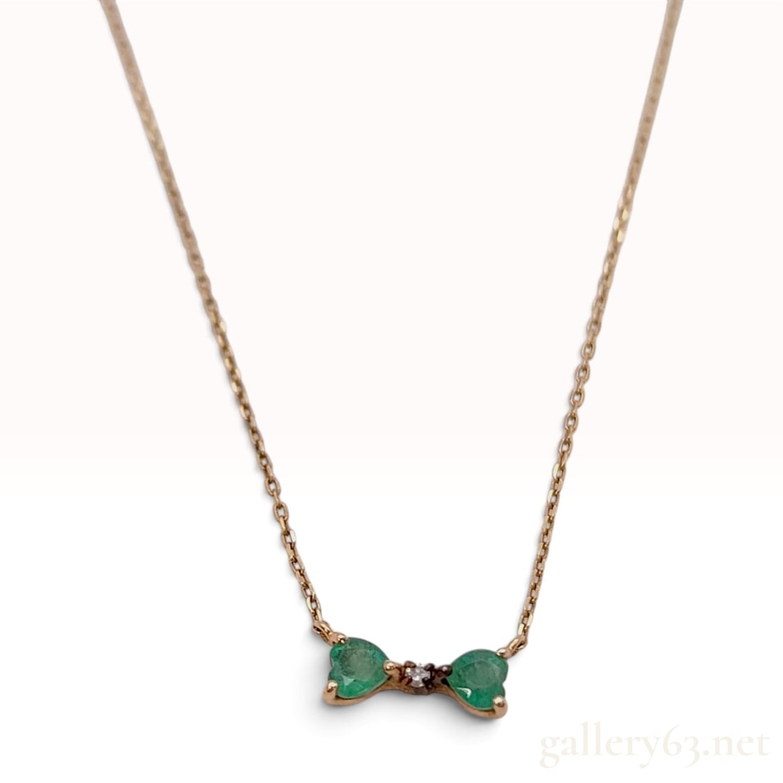 Canal 4 degrees C 10K Yellow Gold Emerald and Natural Diamond Bow Necklace: A Canal 4 degrees C necklace featuring a fixed bow-motif pendant crafted from 10K yellow gold. The decorative pendant is set with two heart-shaped faceted emeralds that form the loops of the bow, each