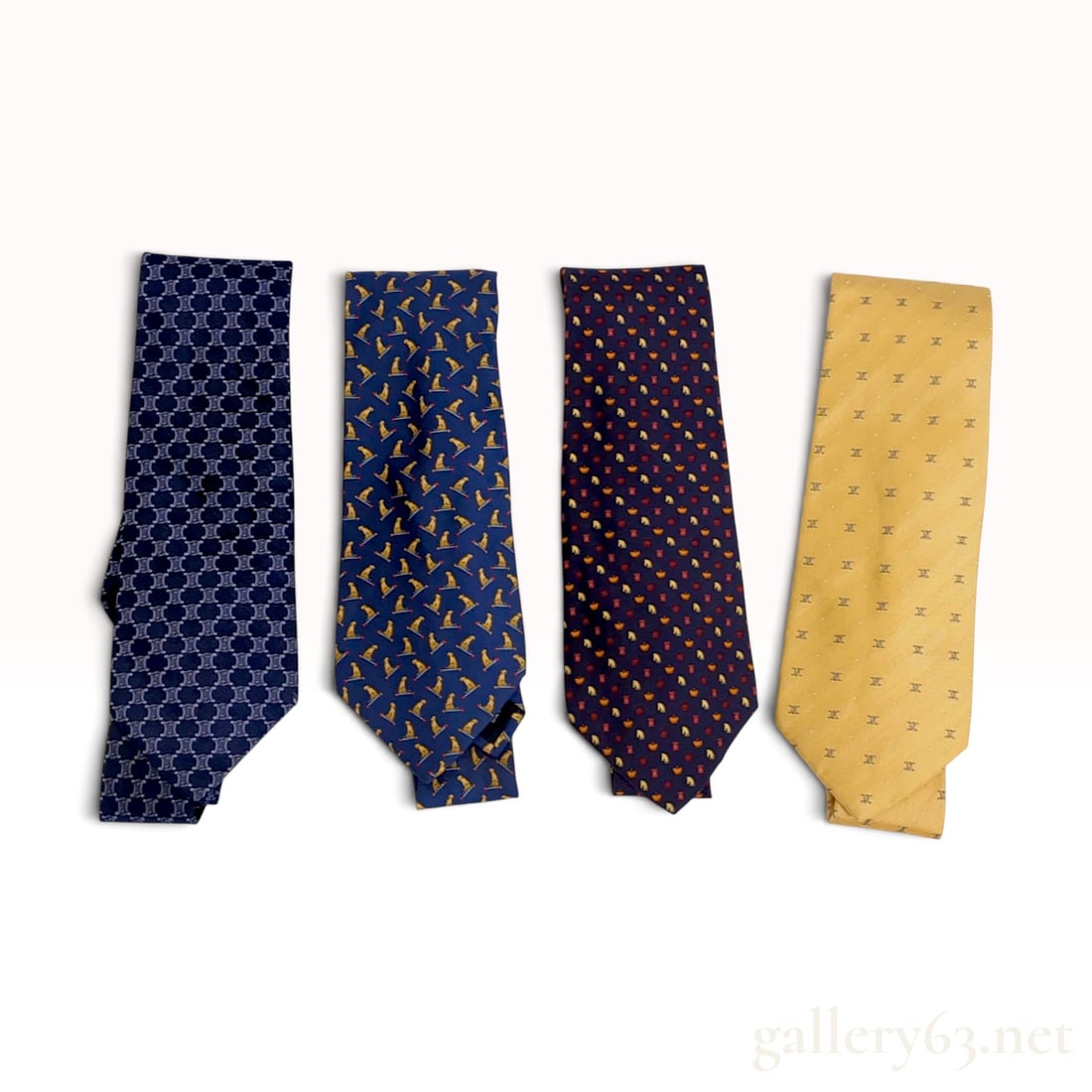 An Assortment of Four Celine and Salvatore Ferragamo Silk Neckties: This assortment of four designer silk neckties includes two examples by Celine and two by Salvatore Ferragamo. The first Celine tie is crafted from blue silk with a repeating grey Macadam pattern. The