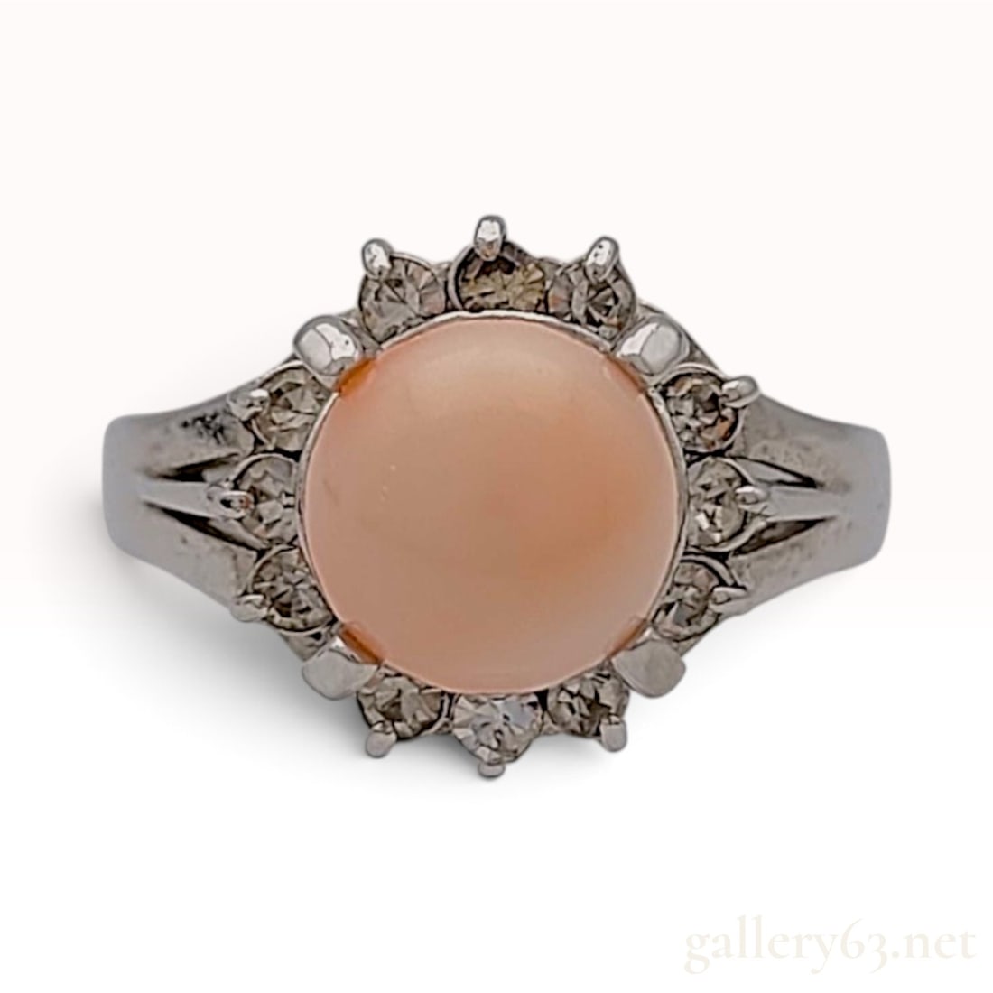 A Vintage Sterling Silver and Peach-Pink Cabochon Cocktail Ring Size 11: This is a vintage sterling silver cocktail ring featuring a large peach-pink cabochon centerpiece. The round cabochon is held by four decorative prongs and is surrounded by a halo of twelve colorless 