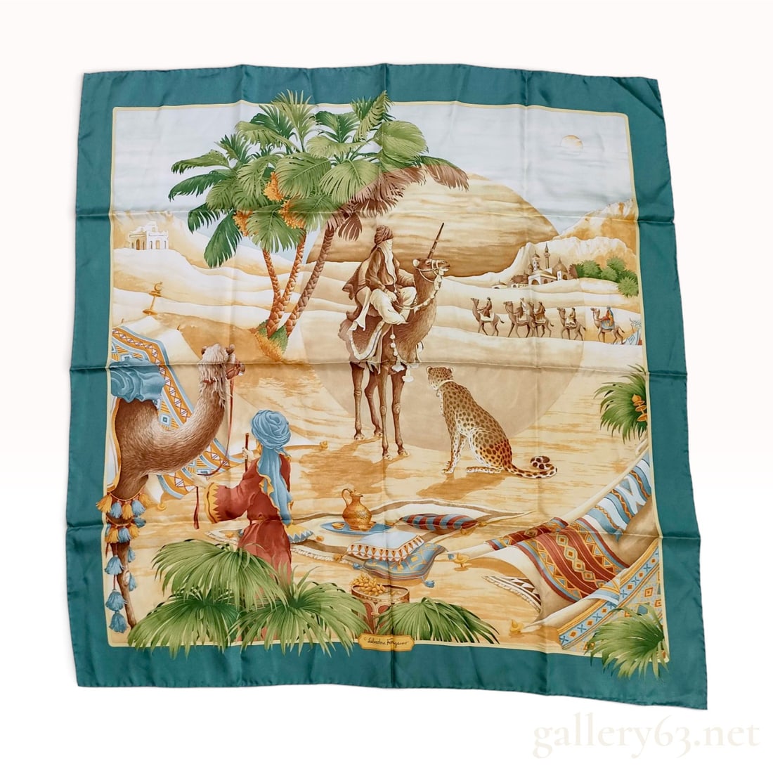 Salvatore Ferragamo Touareg Desert Oasis Teal Silk Scarf 90 cm: This Salvatore Ferragamo silk scarf features an intricate pictorial scene depicting a desert oasis in shades of teal, sand, and ochre. The central composition illustrates a man in traditional attire r