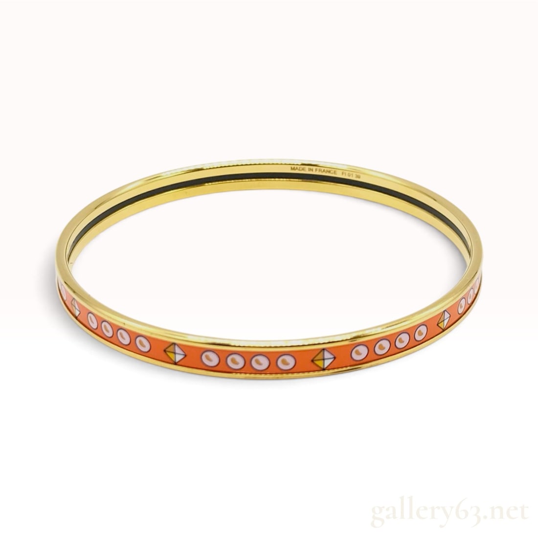 Hermes Orange Enamel and Gold Plated Bangle: This Hermes bangle is crafted from gold-plated metal featuring a signature orange enamel inlay. The enamel band is decorated with a repeating geometric pattern consisting of white circular eye motifs 