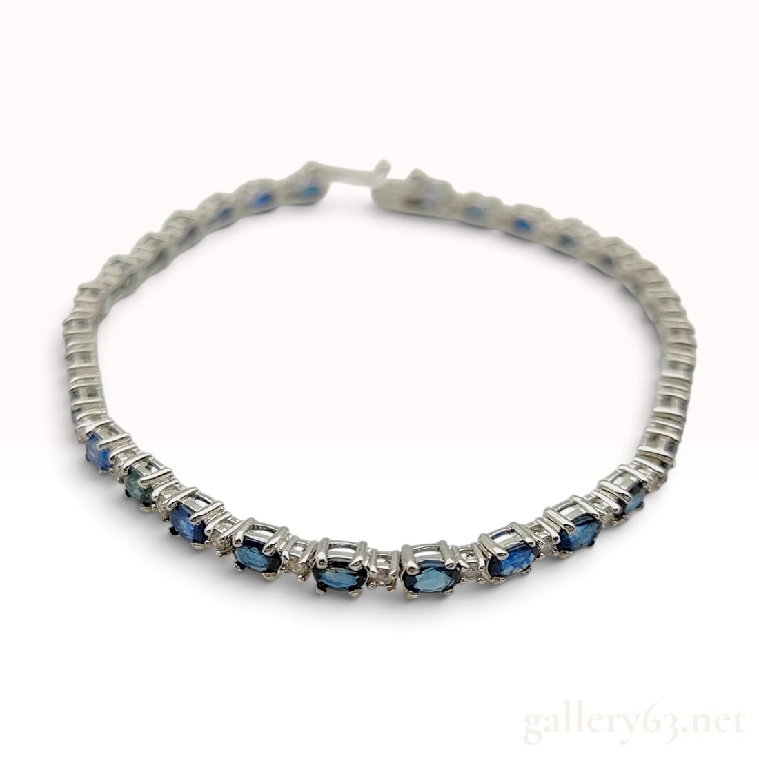 18KWG 9.50ct Sapphire and 0.50ctw Natural Diamond Tennis Bracelet: This tennis bracelet is crafted from 18 karat white gold and features a continuous line of approximately 40 oval-cut blue sapphires. The sapphires are individually prong-set, alternating with pairs of