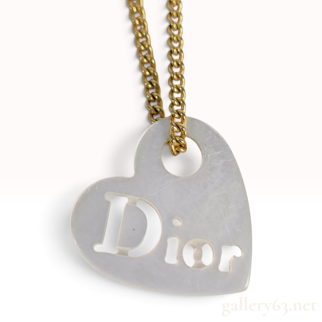 Christian Dior Heart Shell Logo Gold Tone Pendant Necklace: A Christian Dior pendant necklace featuring a heart-shaped iridescent shell pendant. The pendant design includes a stylized openwork cutout of the Dior name. The piece is suspended from a gold-toned m