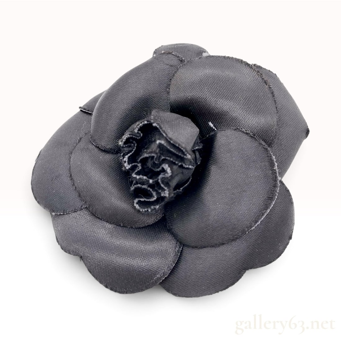 Chanel Camellia Black Fabric Brooch: This Chanel Camellia brooch is crafted from black textile with a satin finish, featuring layered petals constructed into a three-dimensional floral motif. The fabric petals are die-cut with raw edges 