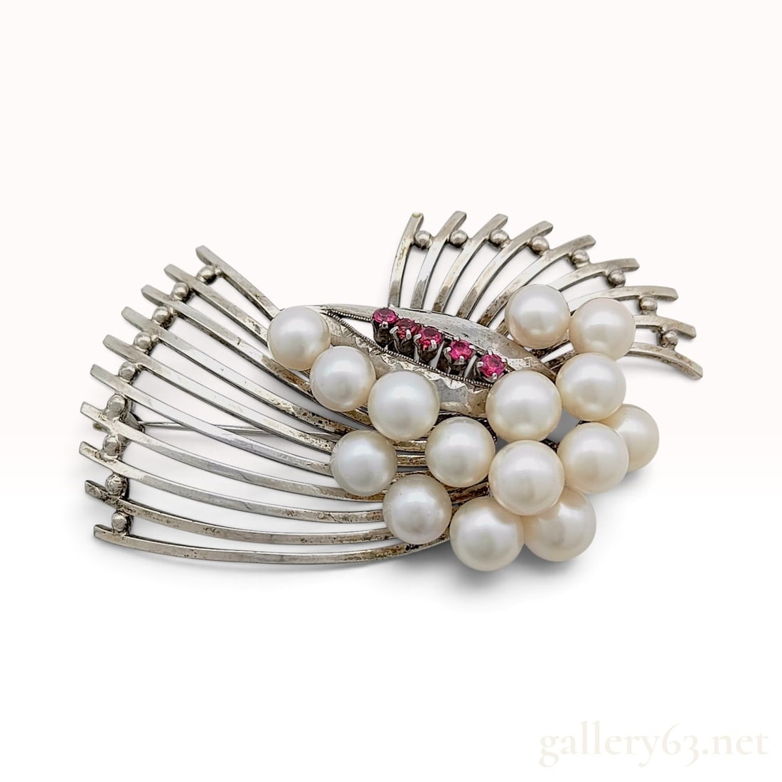 Sterling Silver 13 Cultured Pearl and Ruby Spray Brooch: This mid-century modern spray brooch is crafted from sterling silver and features a cluster of thirteen round white cultured pearls. The pearls exhibit a white body color with pinkish overtones and ar